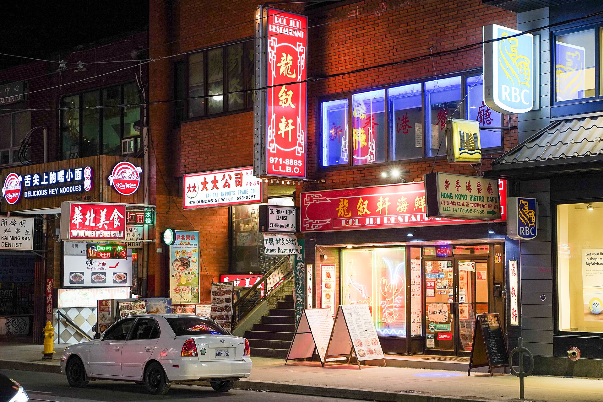 Restaurants with Chinese and English signs lit up at night on a Toronto Chinatown street